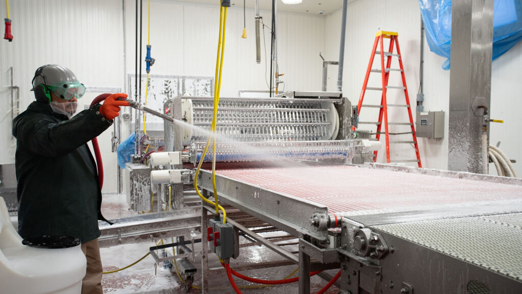man spraying food conveyor with foam product